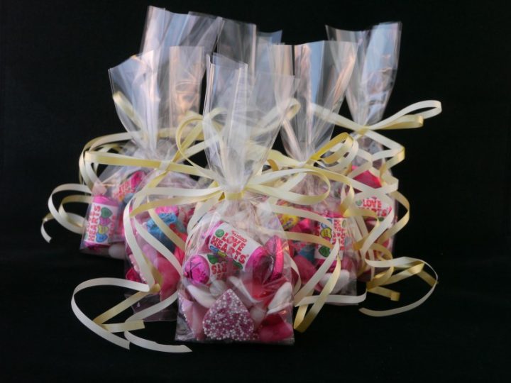 A group photo of several wedding favour bags tied with gold ribbons and filled with love heart sweets, jelly heart sweet and chocolate heart sweets